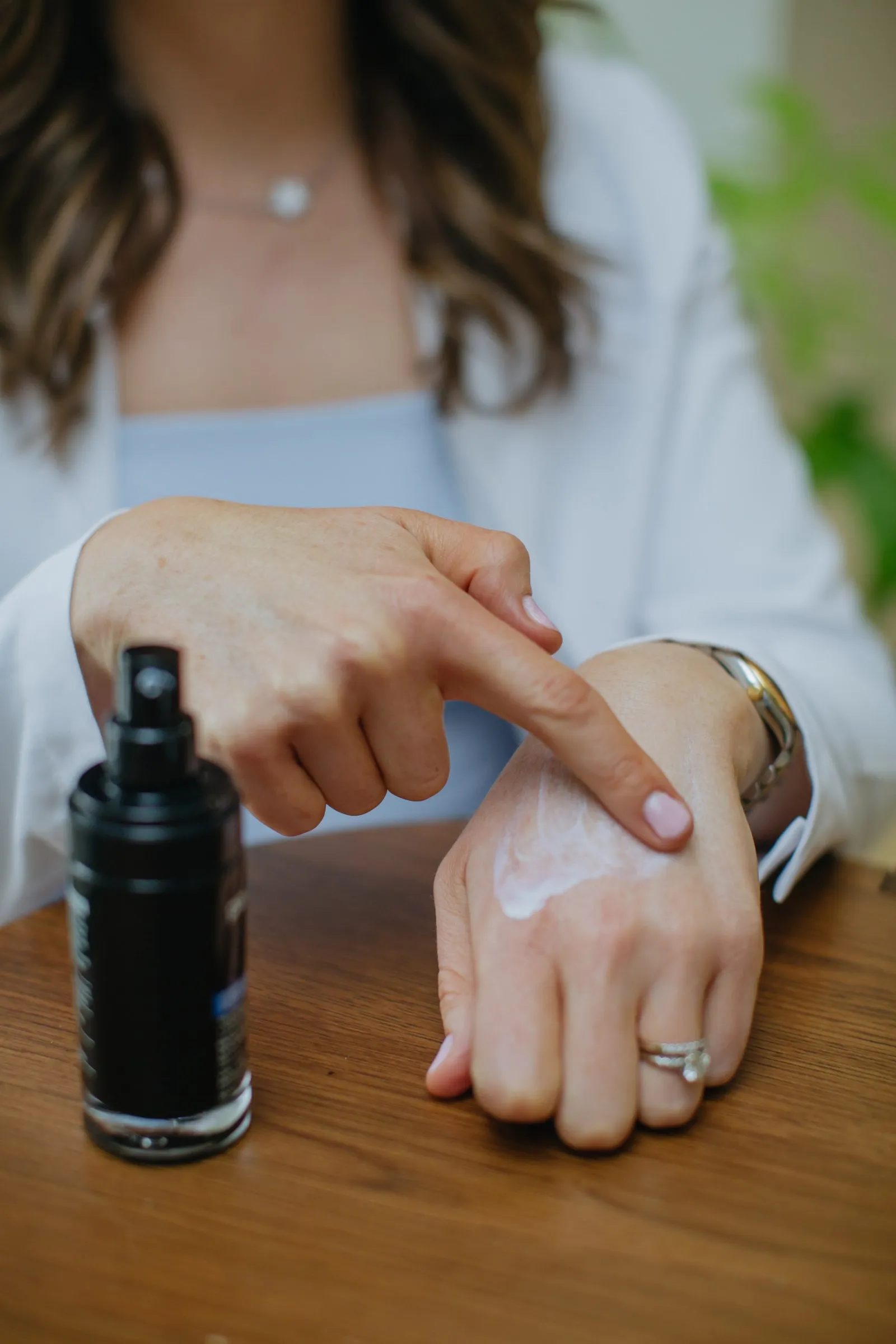 A fingertip applying skincare cream to the back of a hand beside a black SkinBetter bottle on a wood table