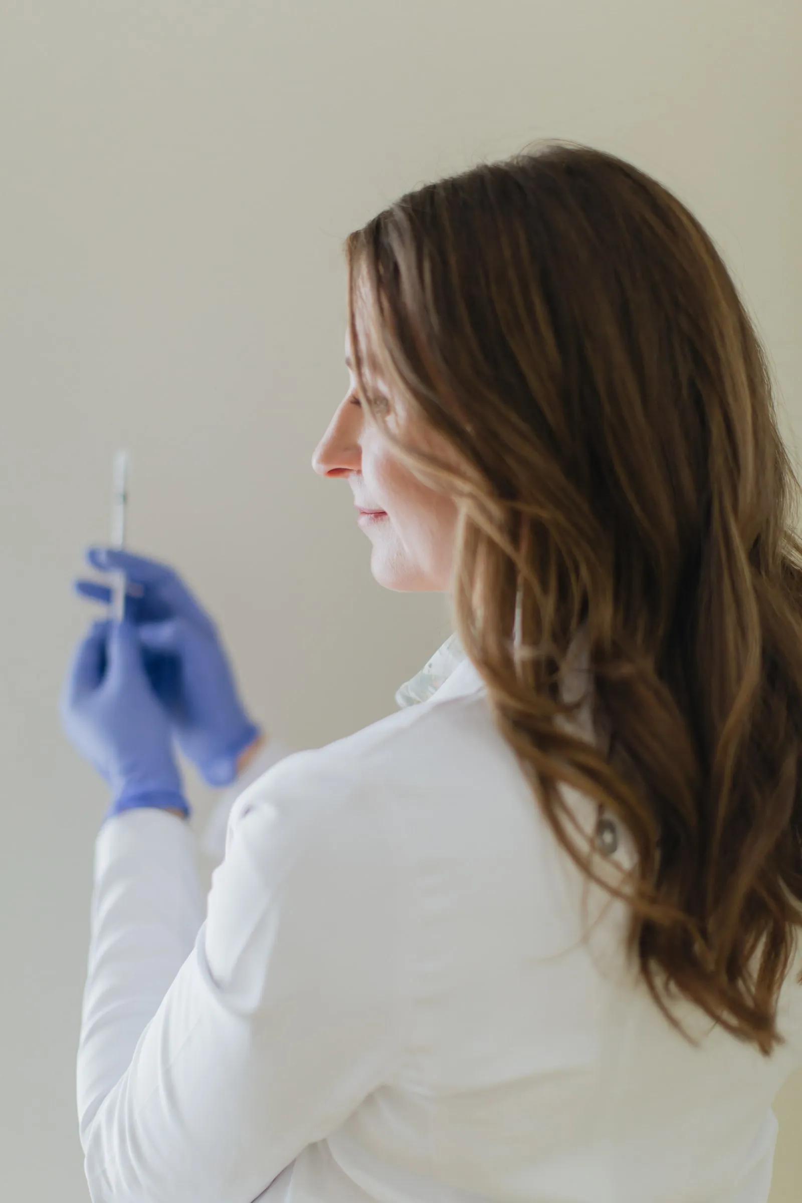 Danielle Wise, NP, in profile inspecting a syringe against a plain wall
