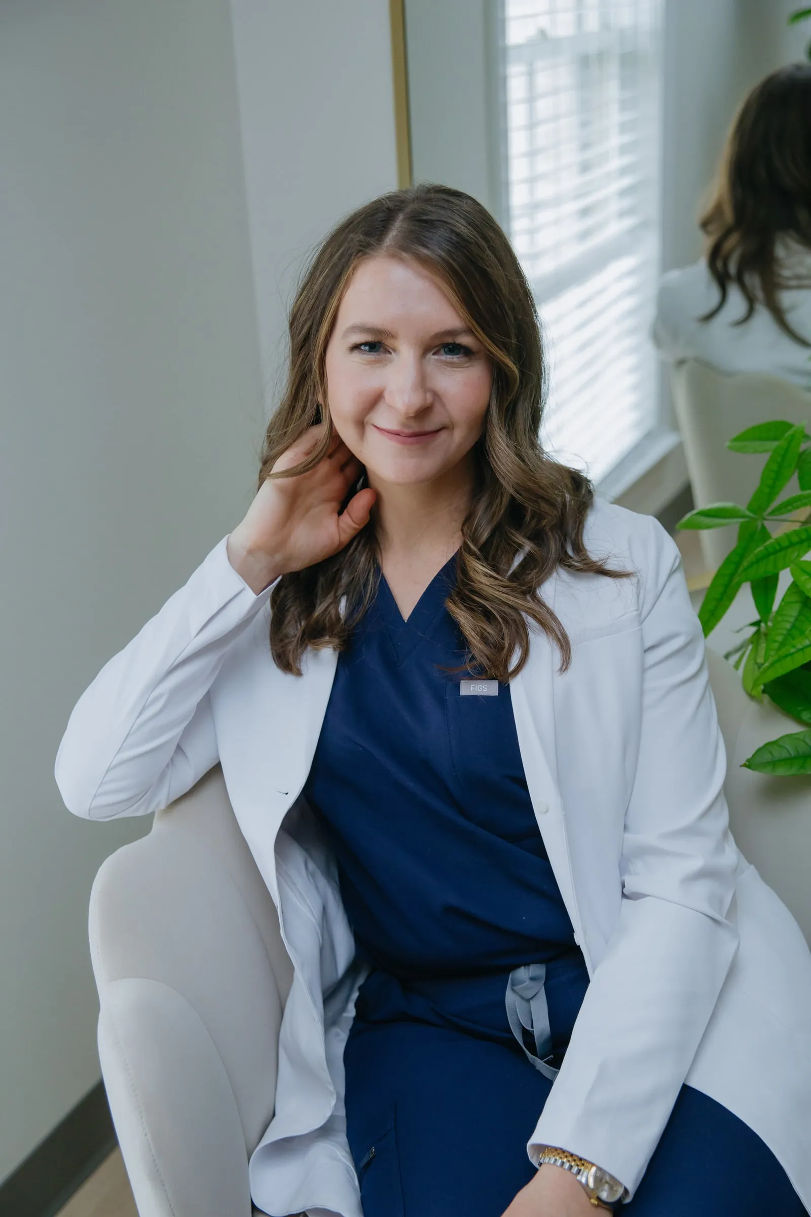 Danielle Wise, NP, in a white coat seated by a window, smiling directly at the camera