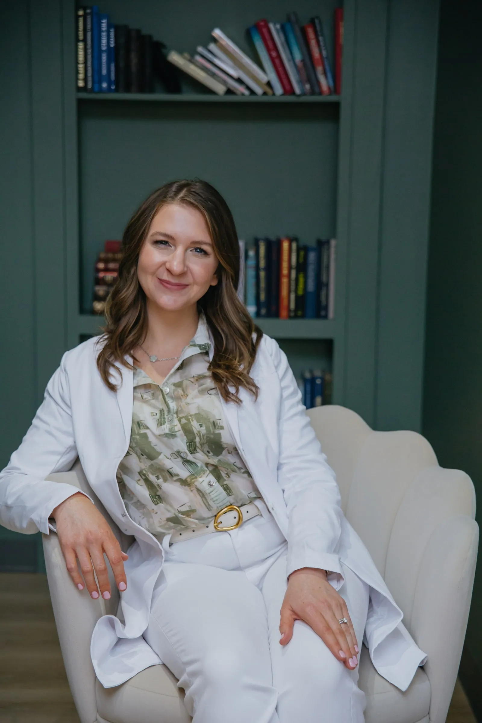 Danielle Wise, NP, in white, seated before the studio's green bookshelf